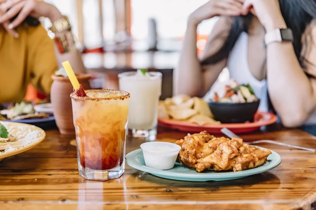 Restaurant table with drinks, sauced chicken, ceviche, and people.