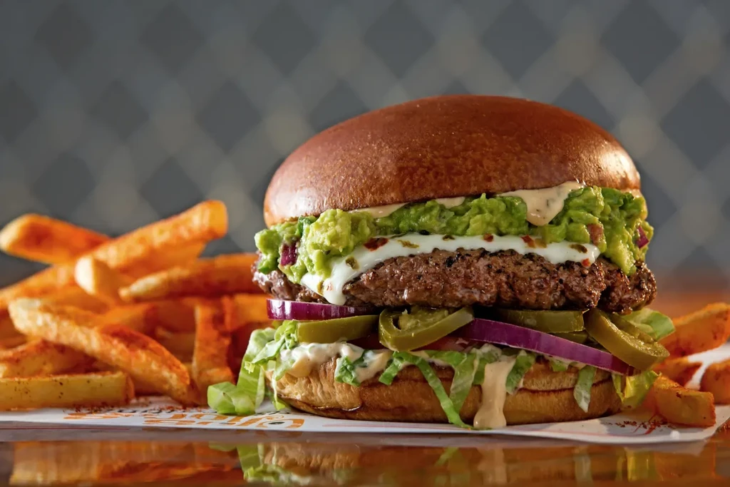 Gourmet burger with guacamole, cheese, and fries on a dark background.