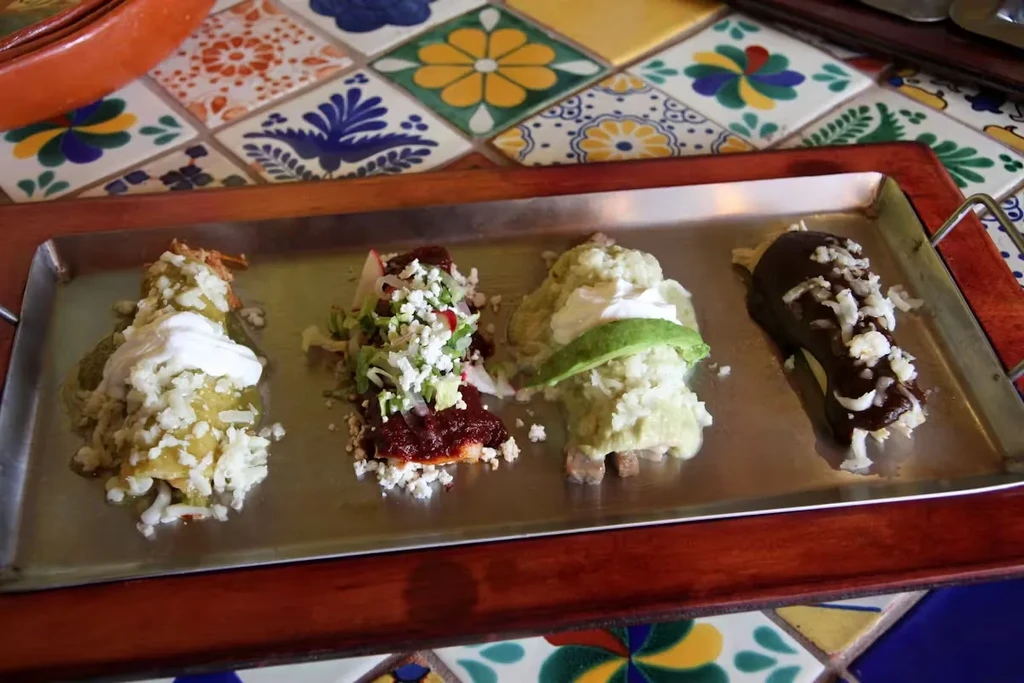 Four enchilada portions on a metal tray, each with different toppings.