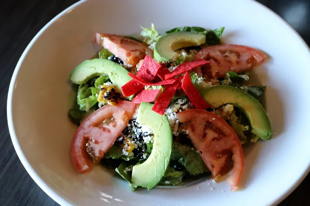 Vibrant salad with greens, tomatoes, avocado, black beans, cheese.