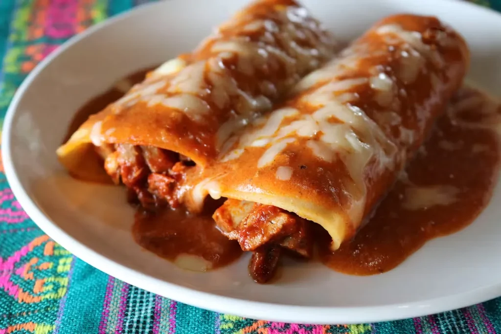 Two enchiladas topped with orange sauce and melted white cheese.