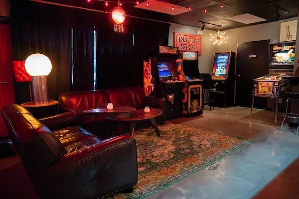 Dimly lit entertainment lounge with leather couches, arcade machines, and red lighting.