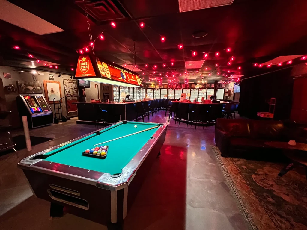 Dimly lit bar with pool table, Lone Star sign, and red lights.