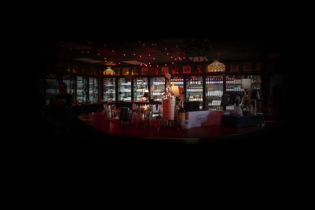 Dimly lit bar interior with shelves of alcoholic beverages.