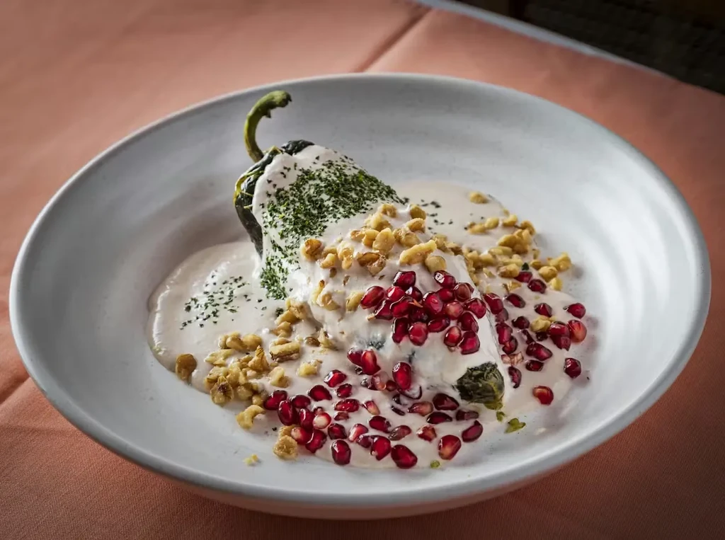 Chiles en Nogada dish in a bowl, garnished with walnuts and pomegranate.