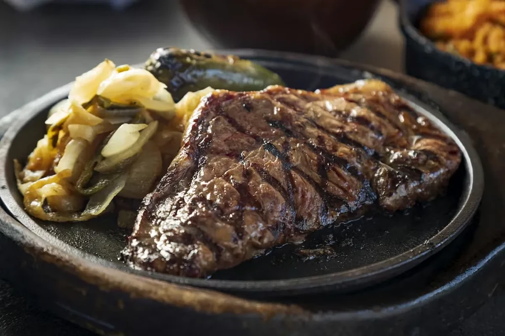 Grilled steak, sautéed onions, roasted pepper on a sizzling plate.