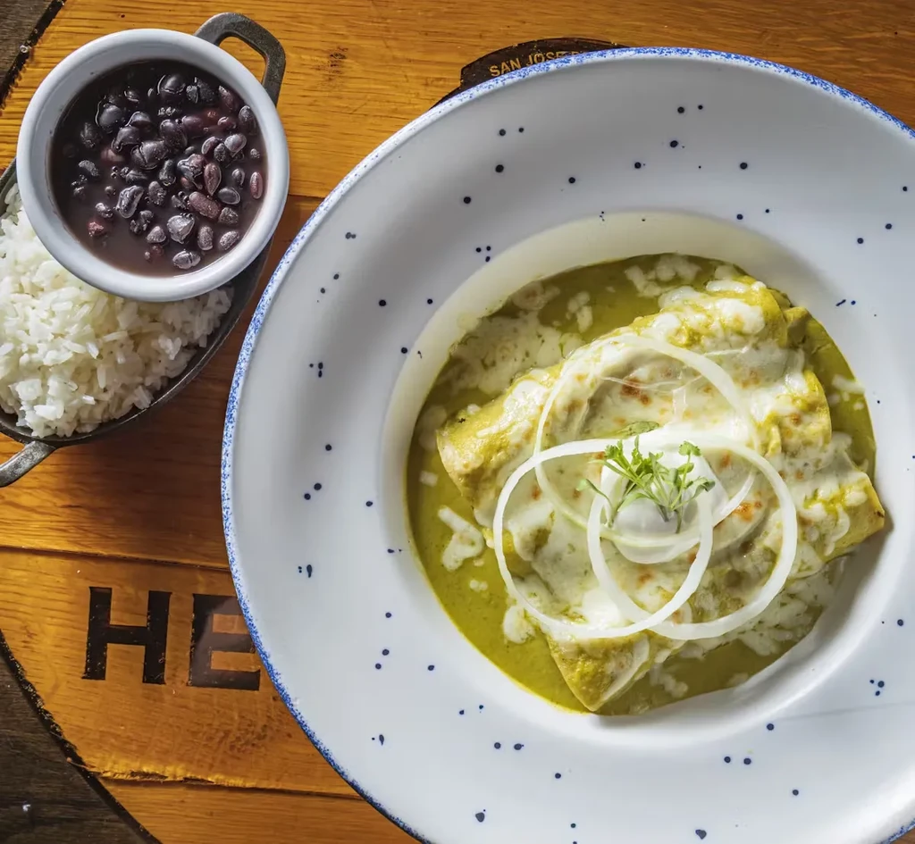 Green enchiladas with rice and beans on a wooden table.