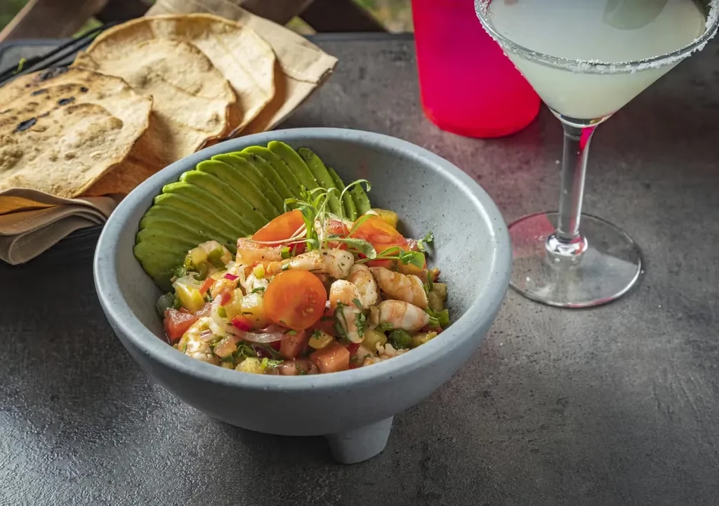 Ceviche bowl with shrimp, vegetables, avocado, tortillas, and drink.