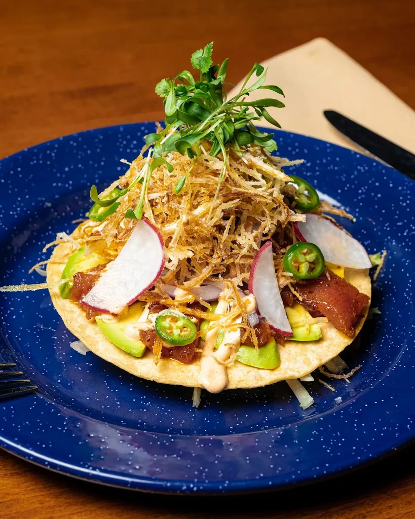 Close-up of a tostada with various toppings on a dark blue plate.