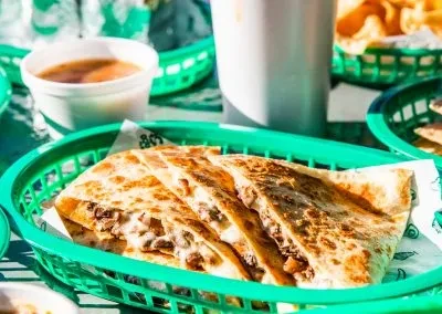 Meat and cheese quesadilla slices in a green basket with salsa.