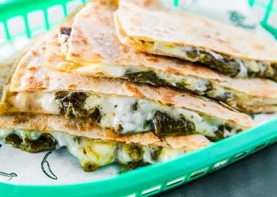 Stacked golden-brown quesadillas with gooey cheese and green filling in a basket.