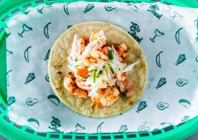 Shrimp taco, seasoned shrimp, slaw, pico de gallo, in green basket.