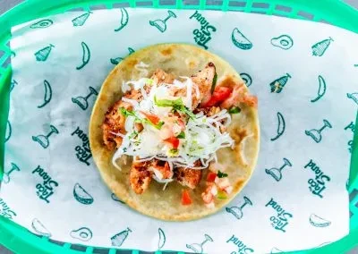 Single grilled chicken taco with cabbage and pico de gallo in green basket.