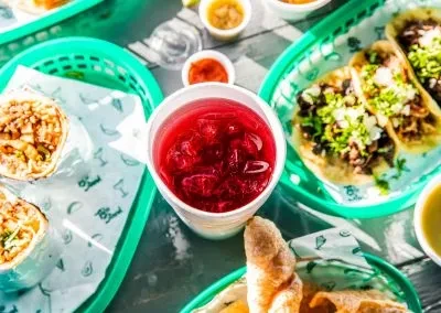 Burritos, tacos, and a red drink served with condiments on a table.