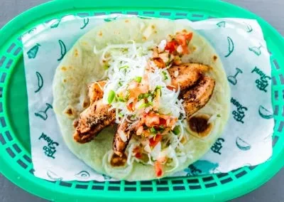 Open fish taco with cabbage, salsa, and green onions in a basket.