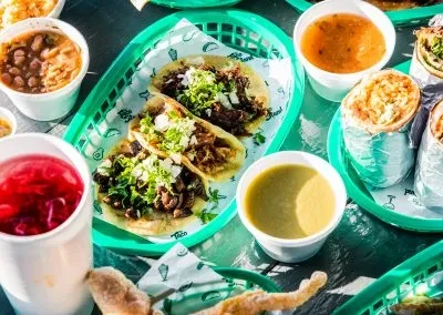 Overhead view of Mexican tacos, burritos, sauces, and a red drink.