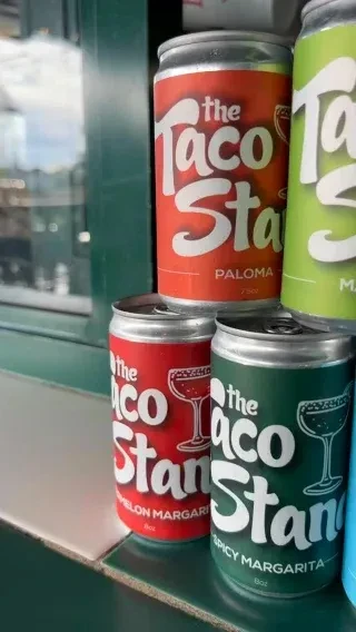 Vibrant 'The Taco Stand' canned margaritas and palomas on a counter.