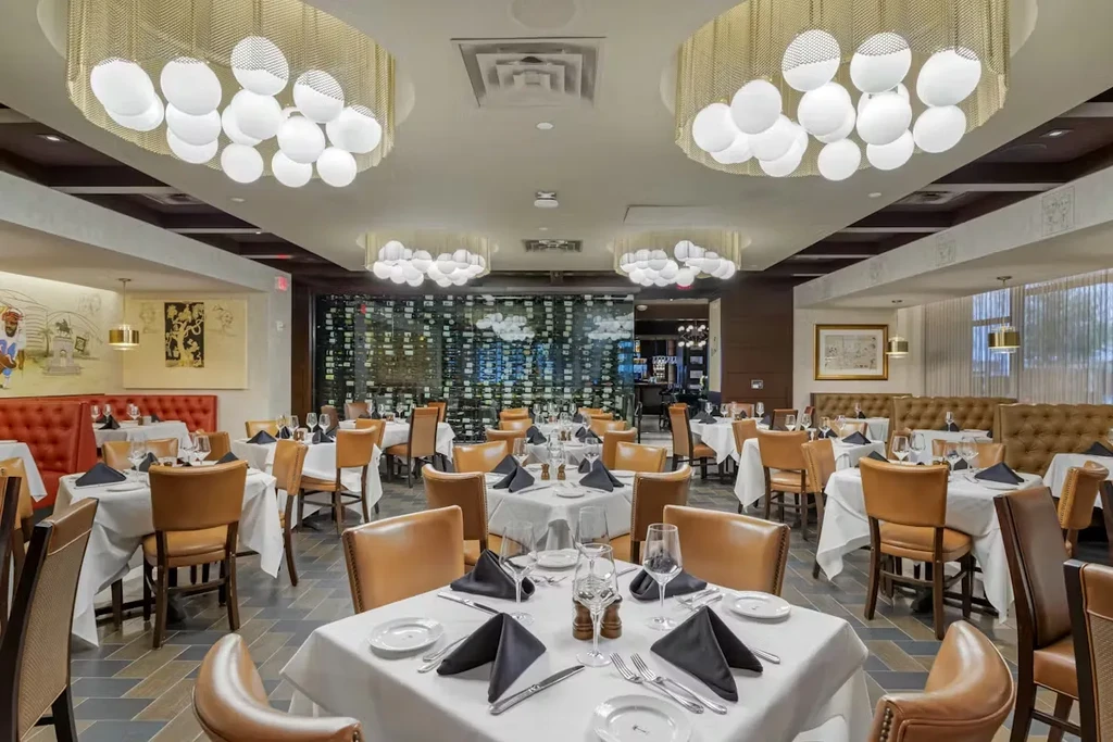 Upscale restaurant dining area with elegant tables, chandeliers, and a wine display.