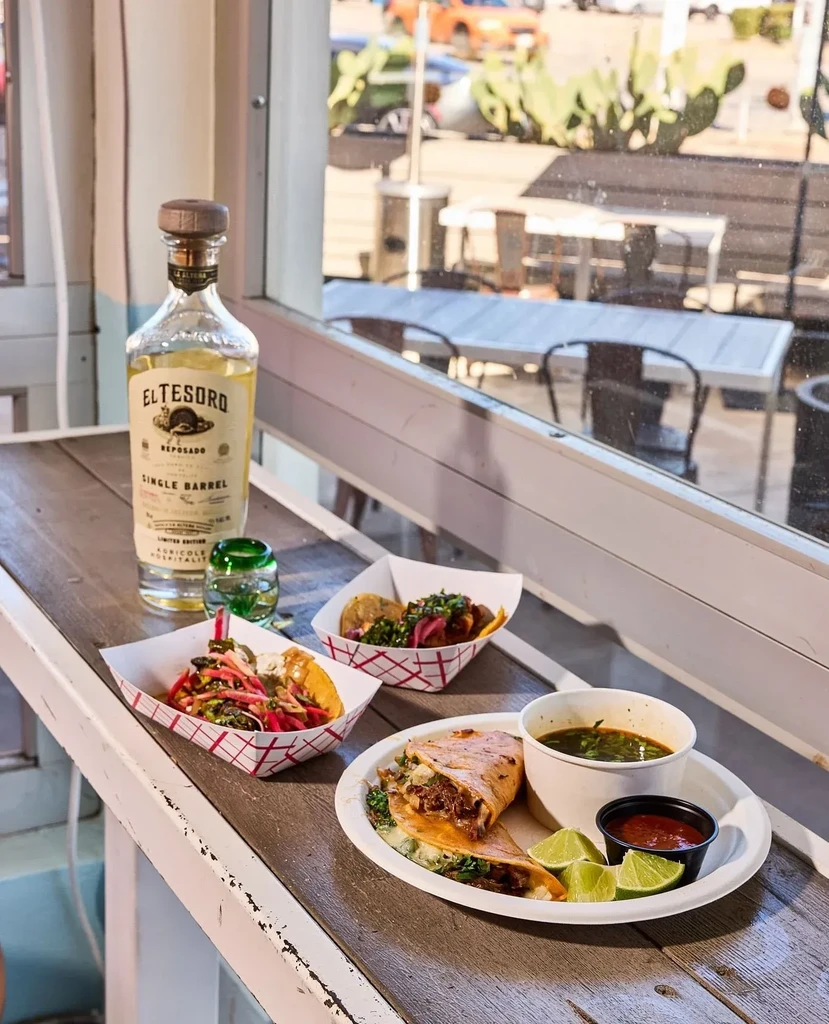 Mexican food, tequila, and consommé on a rustic wooden surface.