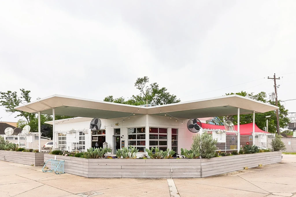 Modern white building with awning, outdoor fans, and desert plants.