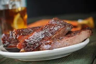 Close-up of several barbecued ribs with a dark, glossy sauce.