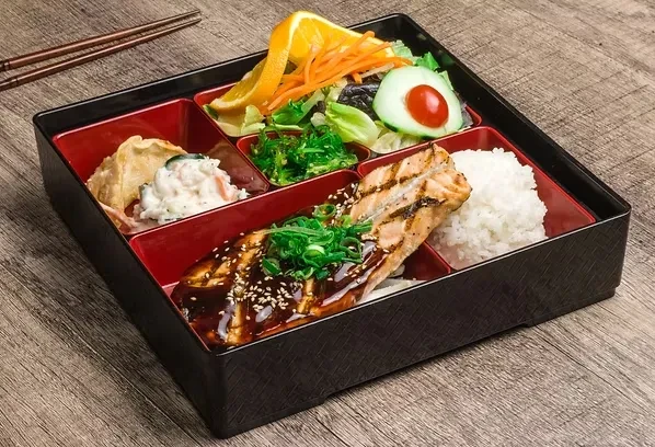 Japanese bento box with salmon, rice, salad, and dumplings.