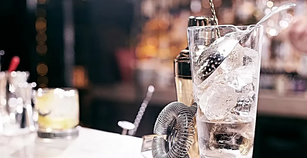 Close-up of bartender's station with cocktail tools, shaker, and drinks.