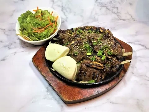 Grilled short ribs, buns, and salad on a marble surface.
