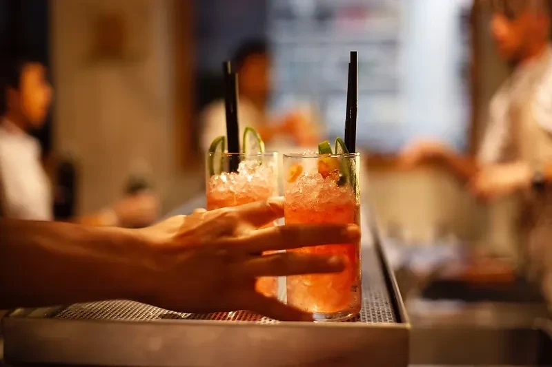 Two reddish-orange cocktails with ice and lime on a metallic tray.