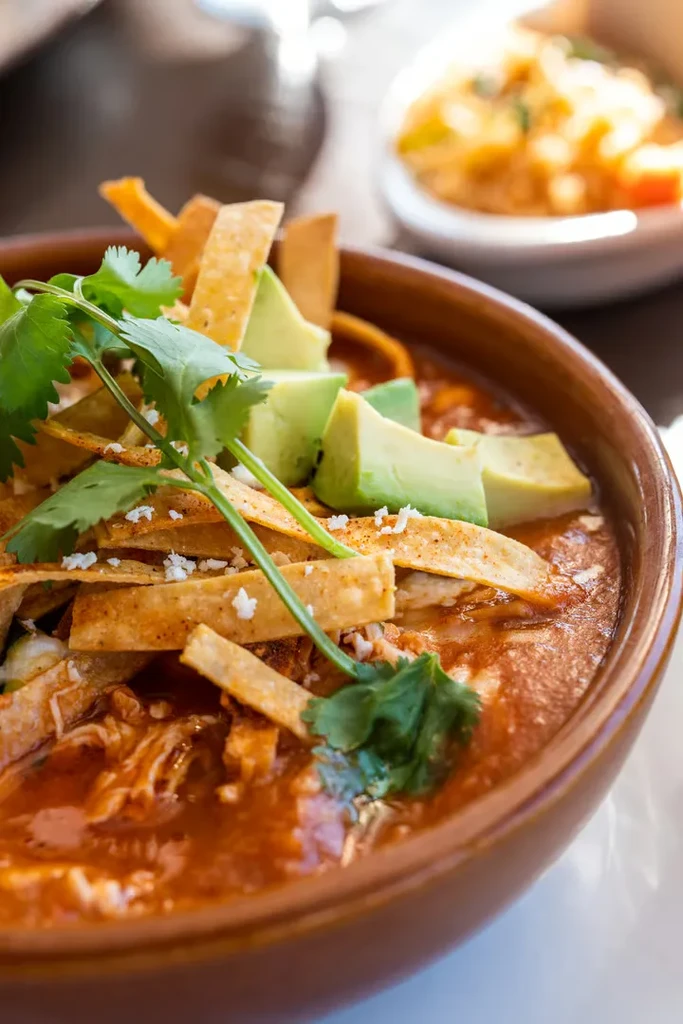 Bowl of tortilla soup with chicken, avocado, and tortilla strips.