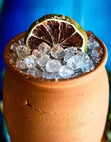 Terracotta pot filled with ice, a dried lime slice, and a blue background.