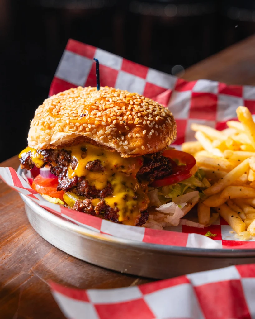 Double cheeseburger with fries on a red and white checkered paper.