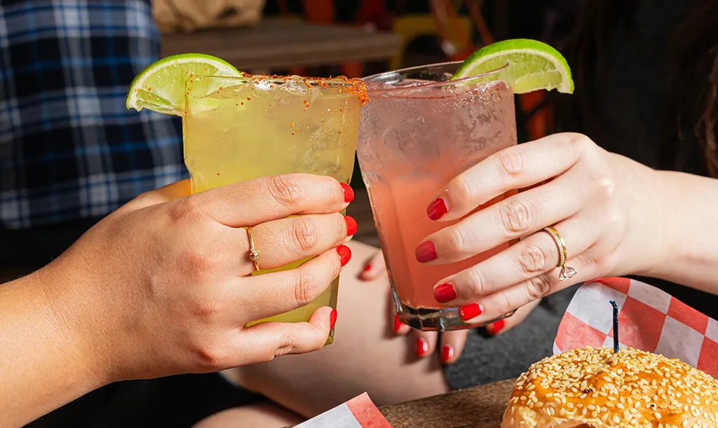 Two people toast drinks with chili-salt and lime in a restaurant.