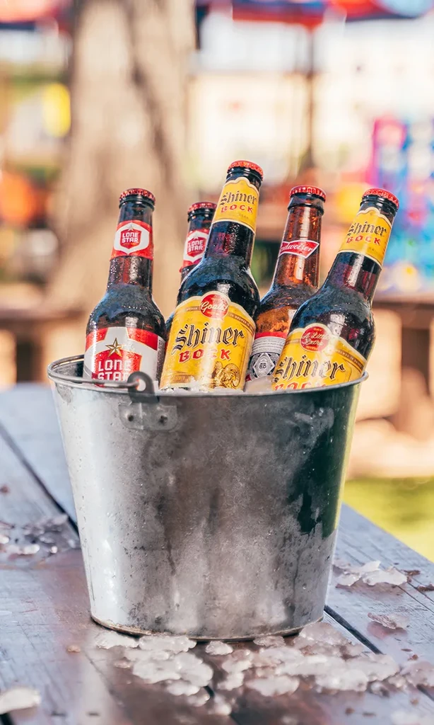 Galvanized bucket of ice and beer bottles on a wooden table.