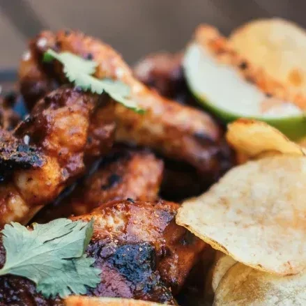 Grilled chicken wings with a dark sauce, cilantro, lime, and chips.