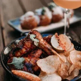 Chicken wings, potato chips, lime wedge, and cilantro in a dark bowl.