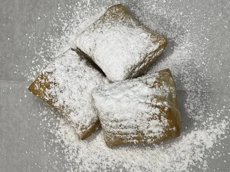 Three golden-brown pastries generously dusted with white powdered sugar.