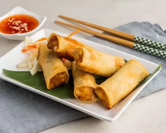 Fried spring rolls with cabbage, carrots, dipping sauce, and chopsticks.
