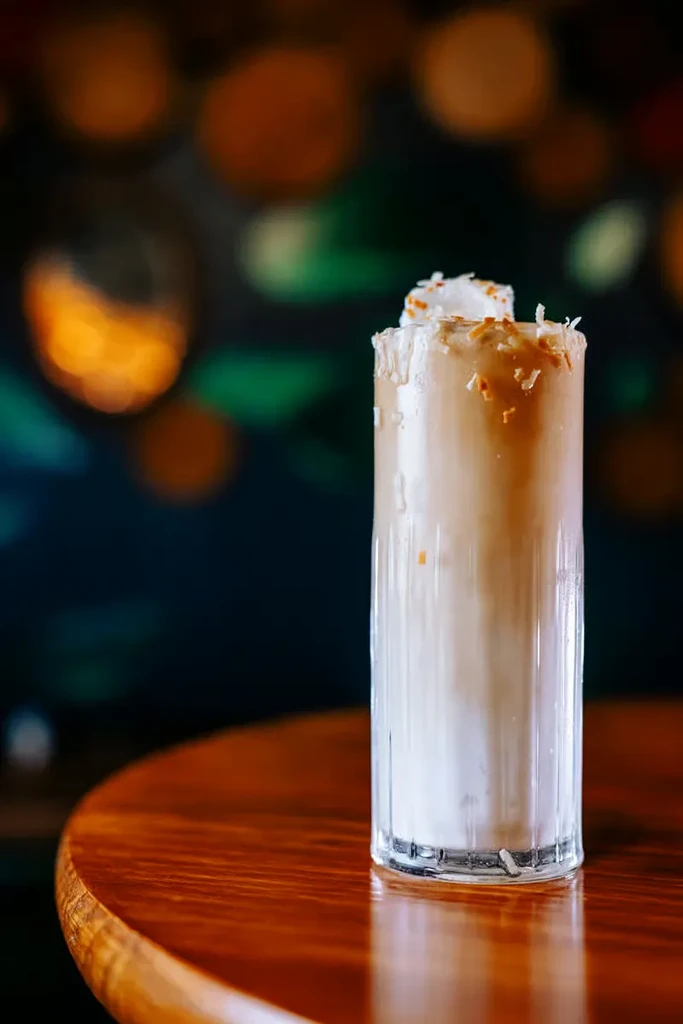 Two-toned drink with whipped cream and toasted flakes on wood.