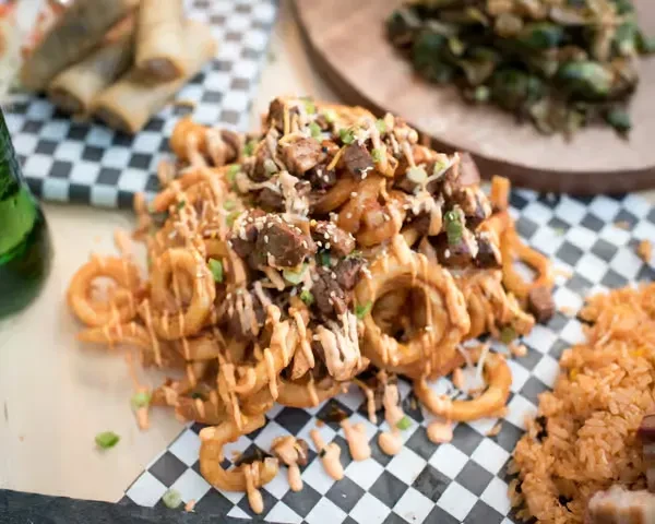 Close-up of curly fries topped with meat, sauce, and green onions.