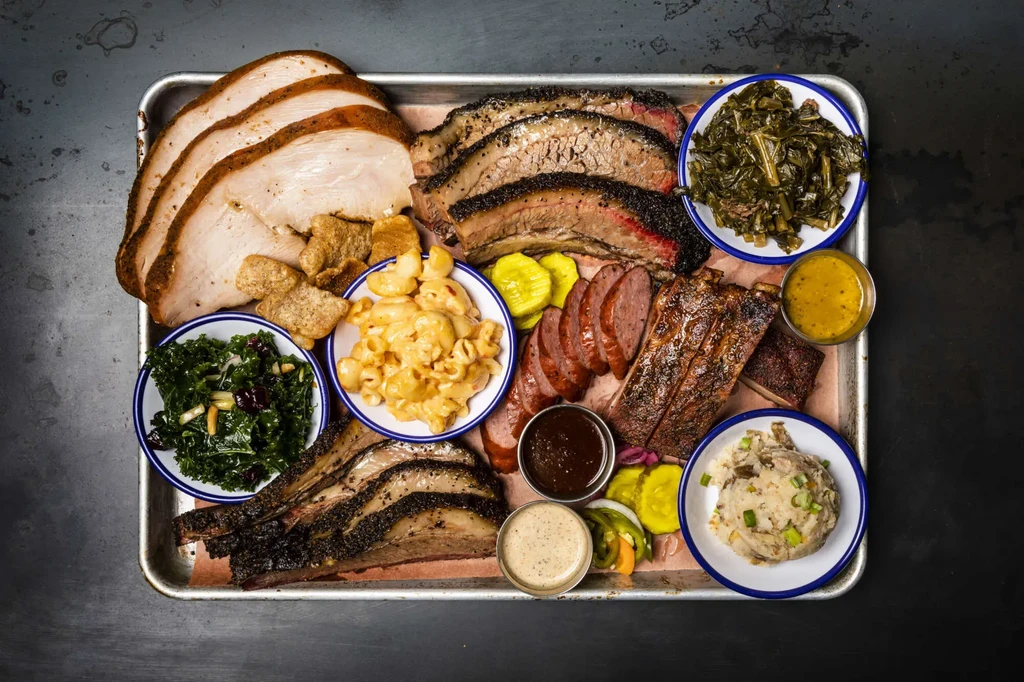 Metal tray of barbecue meats and sides on butcher paper.