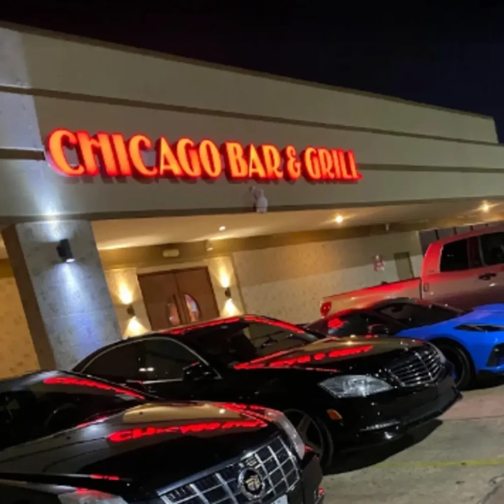 Exterior of "CHICAGO BAR & GRILL" at night with parked cars.