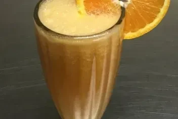 Fluted glass with an orange drink, frothy head, and orange slice.