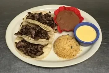 Three meat tacos, refried beans, queso, and rice on a plate.