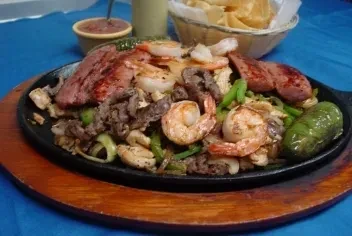 Sizzling fajita platter with shrimp, beef, peppers, and onions.