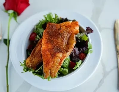Fish fillets on salad with cherry tomatoes and a rose.