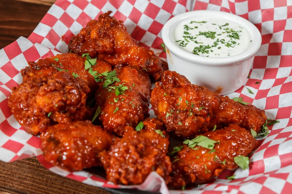 Close-up of hot wings in a basket with dipping sauce.
