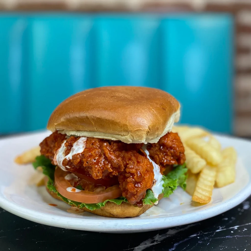 Spicy chicken sandwich with lettuce, tomato, sauce, and fries.