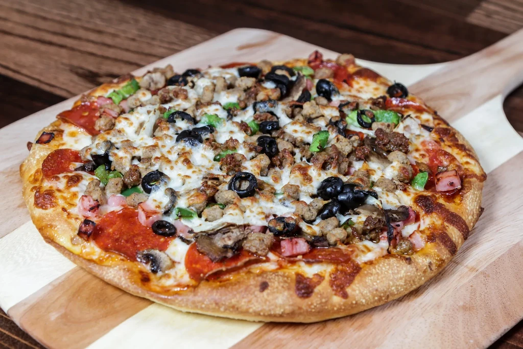 Fully baked pizza with various toppings on a wooden peel.