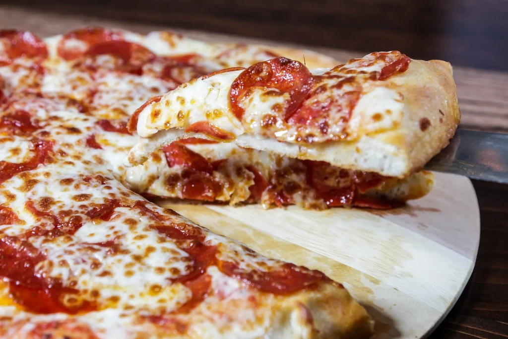 Pizza slice being lifted from a pepperoni pizza on a wooden peel.